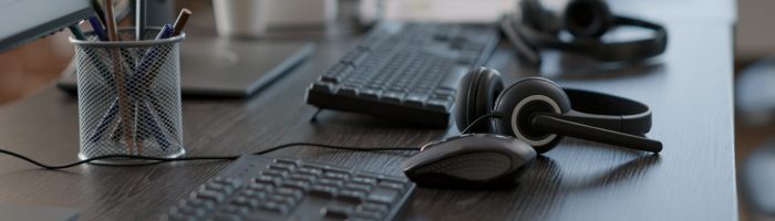 Audio headset used by call center agents to help clients and do telecommunication with technology. Empty customer service workstation with headphones, computers and modern gadgets.